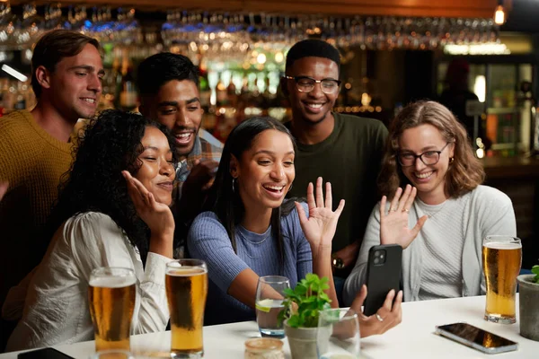 バーで携帯電話でビデオ通話を行うカジュアルな服を着て友人の幸せな若い多人種グループ — ストック写真