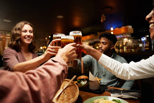 快乐的年轻多种族的朋友们穿着休闲装在酒吧里和啤酒一起举杯 — 图库照片