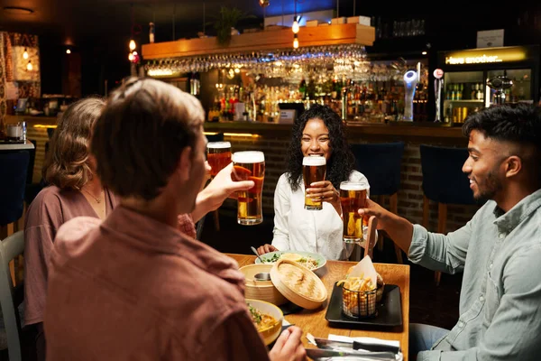 快乐的年轻多种族的朋友们穿着休闲装坐在酒吧里吃饭喝酒 — 图库照片