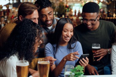 Barda cep telefonu kullanarak gündelik giysiler giyen mutlu, çok ırklı bir arkadaş grubu.