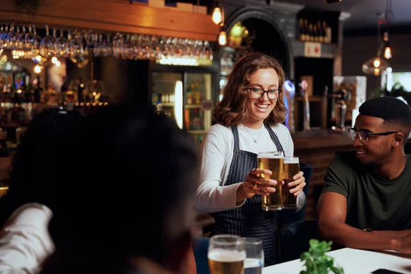 バーでウエイトレスからビールを受け取るカジュアルな服を着ている友人の幸せな若い多人種グループ — ストック写真