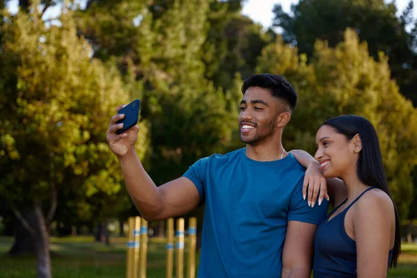 Happy young multiracial couple wearing sportswear smiling while taking selfie with mobile phone in park