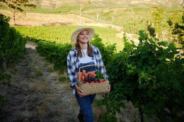 穿着休闲装 提着一篮子水果和蔬菜在农场里散步的快乐年轻的高加索女人 — 图库照片