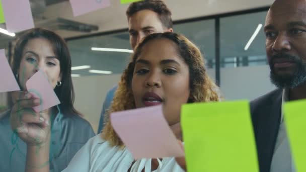 オフィスでのミーティング中に多色の粘着性のあるノートを使用しながら話す多種多様なビジネスのグループ — ストック動画