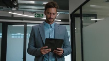 Şirketin koridorunda yürürken dijital tablet kullanan Kafkasyalı genç adam.