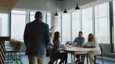 Bir grup çok ırklı iş arkadaşı ofiste iş görüşmeleri sırasında selamlaşıp tartışıyorlar.