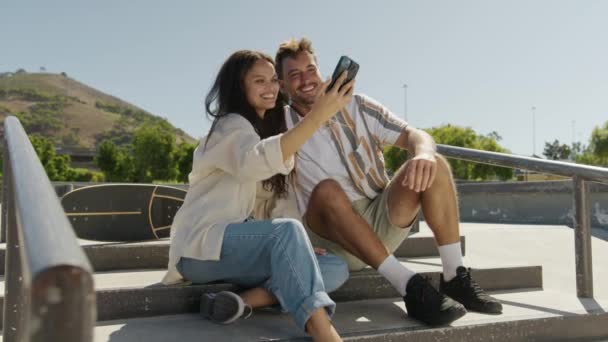 スケートパークで携帯電話でセルフィーを取るカジュアルな服を着ている若い多人種カップル — ストック動画