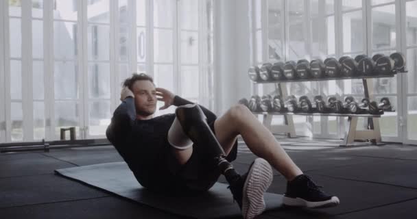 ジムで座っている義足でスポーツウェアの若い白人男性を決定 — ストック動画