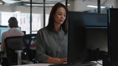 Şirket ofisinde masa başında bilgisayar kullanan beyaz gömlekli genç bir kadın.