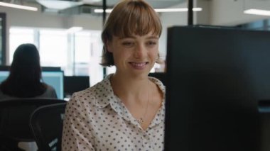 İş hayatında beyaz kadın şirket ofisindeki masada bilgisayar kullanırken gülümsüyor.