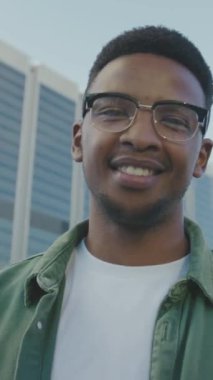 Sıradan kıyafetler giyen, gülümseyen ve kollarını kavuşturmuş kameraya bakan genç siyahi bir adamın portresi.