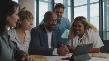 Ofisteki dijital tablet toplantısında gülümseyen ve alkışlayan çok ırklı meslektaşlar grubu