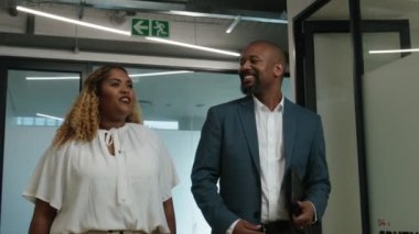 Olgun siyahi adam ve orta yaşlı siyahi kadın şirket ofisinde konuşuyor ve el kol hareketi yapıyorlar.