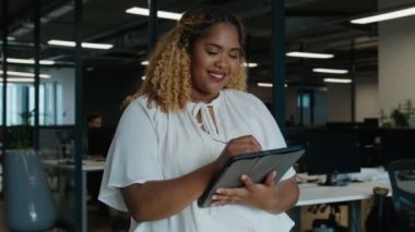 Orta yaşlı mutlu siyahi kadın şirket ofisindeki masanın yanında dijital tablete yazı yazıyor.