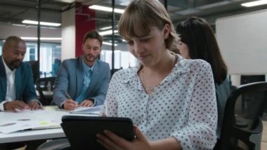 Şirket toplantısı sırasında dijital tablet kullanırken gülümseyen çok ırklı iş arkadaşları grubu