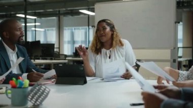 Çalışma odasındaki toplantı sırasında iş kıyafetleri içinde dijital tabletin yanında konuşan bir grup çok ırklı iş arkadaşı.