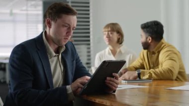 Şirket ofisindeki toplantı sırasında dijital tablet kullanarak iş kıyafetleri giyen dört genç yetişkin.