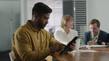 Şirket ofisindeki toplantı sırasında dijital tablet kullanan iş kıyafetleri giyen dört mutlu yetişkin.