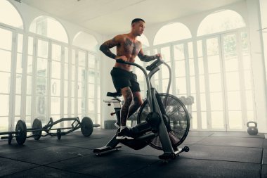 Gömleksiz, dövmeli, şort giyen spor salonunda bisiklet süren çok kültürlü bir genç.