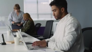 İş kıyafetleri giyen genç yetişkinler şirket ofisindeki bilgisayarlarda konuşuyor ve daktilo kullanıyorlar.