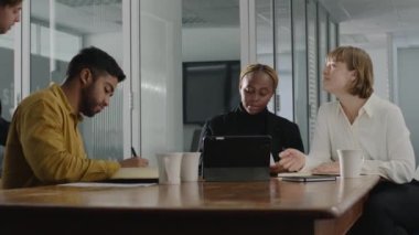 İş hayatında dört genç çok ırklı iş adamı ofislerinde dijital tablet etrafında toplanıyorlar.