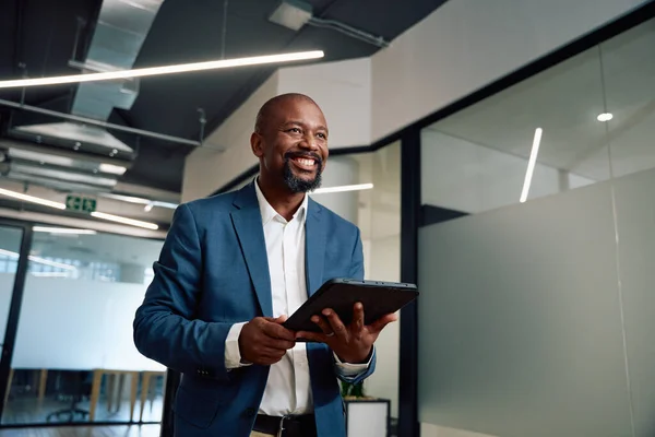 Happy mature black man wearing businesswear with digital tablet in corridor of corporate office