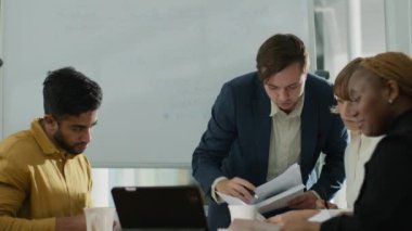 Şirket ofisindeki toplantı sırasında dijital tablet etrafında konuşan dört çok ırklı iş adamı.