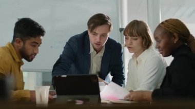 Şirket ofisindeki toplantı sırasında konuşan ve dijital tablet kullanan dört çok ırklı iş adamı.