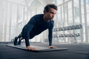 Spor kıyafetleri giyen beyaz bir genç spor salonunda spor minderinde şınav çekerken...