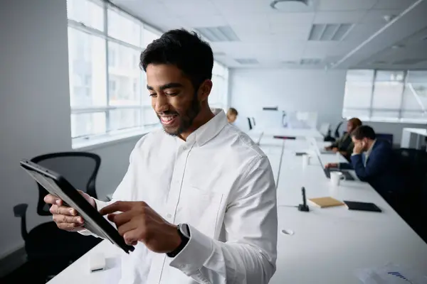 オフィスのデスクでデジタルタブレットを使用してビジネスウェアを着用している幸せな若いビジネスマン ストック画像