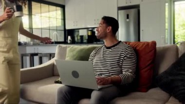 Adam rahat bir şekilde evindeki kanepeye oturmuş bilgisayarını kullanarak dizüstü bilgisayarı, bacağı ve kasları gevşemiş bir şekilde çalışıyor.