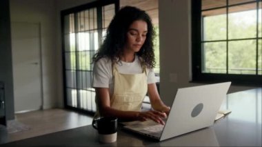 Binanın içindeki bir masada oturan bir kadın, pencerenin yanındaki dizüstü bilgisayarı kullanıyor. Masa tahtadan yapılmış ve dizüstü bilgisayarı da onun kişisel bilgisayarı.