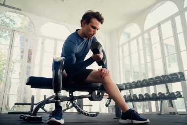 Yapay bacaklı beyaz bir adam spor salonunda halterle halter egzersizi yapıyor.