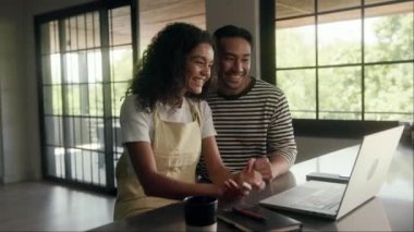 Bir erkek ve bir kadın evin içindeki bir masada dizüstü bilgisayarı paylaşıyorlar. Eğlenirken ekrana doğru gülümser ve hareket ederler. O hamile. Video çağrısı