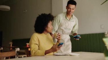 Modern bir kahve dükkanında cep telefonunu kullanarak yemeğini ödeyen Afro-Amerikalı bir müşteri. Yüksek kalite 4k görüntü