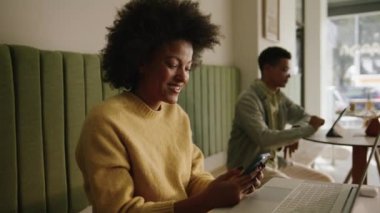 Modern bir kafede cep telefonuyla yazı yazan Afro-Amerikalı bir iş kadını. Yüksek kalite 4k görüntü