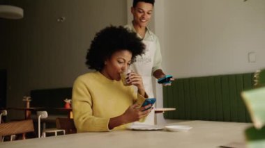 Modern bir kahve dükkanında cep telefonlarını kullanarak yiyecek parasını ödeyen melez bir müşteri. Yüksek kalite 4k görüntü