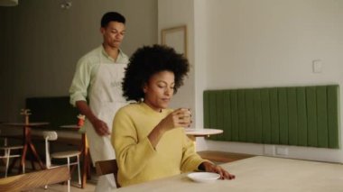 Modern bir kahve dükkanında melez bir müşteriye kruvasan teslim eden Afrikalı Amerikalı bir garson. Yüksek kalite 4k görüntü