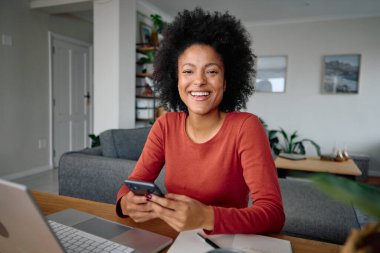 Modern bir dairede ders çalışırken telefonunu tutan Afro-Amerikalı bir kadının fotoğrafı. Yüksek kalite fotoğraf