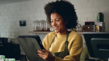 Modern bir kahve dükkanında, tabletin bütçesini Afrikalı Amerikalı kahveci ayarlıyor. Yüksek kalite 4k görüntü