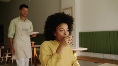 Modern bir kahve dükkanında melez bir müşteriye yemek getiren Afrikalı Amerikalı garson. Yüksek kalite 4k görüntü