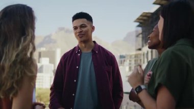 Kendine güvenen genç işadamı, çatıdaki terasta iş arkadaşlarıyla gündüz vakti konuşuyor.