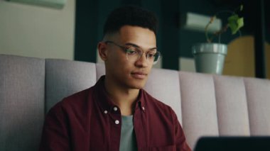 Gündüz vakti modern ofis salonunda dizüstü bilgisayar kullanarak gülümseyen genç işadamı.