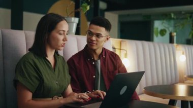 Kendine güvenen işadamı ve iş kadını, modern ofis salonunda otururken dizüstü bilgisayarla tartışıyor.