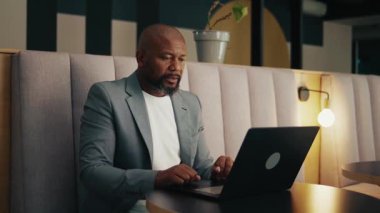 Modern ofis salonunda dizüstü bilgisayarla çalışan siyahi bir işadamı stresli hissediyor