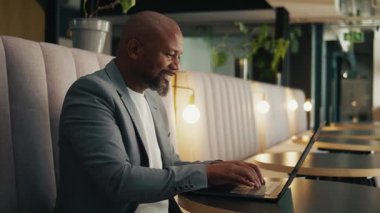 Modern ofis salonunda dizüstü bilgisayar kullanan, spor ceketli, olgun, zenci bir işadamı.