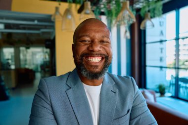 Gündüz vakti modern ofiste kameraya bakarken gülümseyen olgun iş adamının portresi.