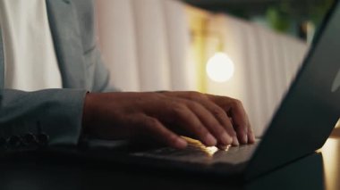 Modern ofis salonundaki dizüstü bilgisayarda yazan takım elbiseli yüzsüz işadamının yakın plan fotoğrafı.