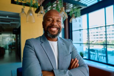 Spor ceketli mutlu bir iş adamının portresi modern ofiste kollarını kavuşturdu.