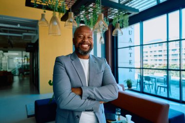 Spor ceketli, neşeli, olgun iş adamının portresi modern ofiste kollarını kavuşturdu.